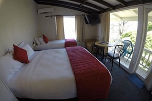 A hotel room with two beds, a small table, chairs, and a balcony with a view. - Colonial Village Motel (Queenstown)
