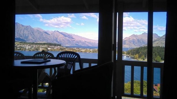 A terrace with a table and chairs, overlooking a lake and mountains.