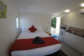 A hotel room with a bed, a red blanket, a towel, a kitchenette, and a balcony. - Colonial Village Motel (Queenstown)