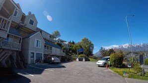 A parking lot with cars, a building with a balcony, and a mountain in the background.