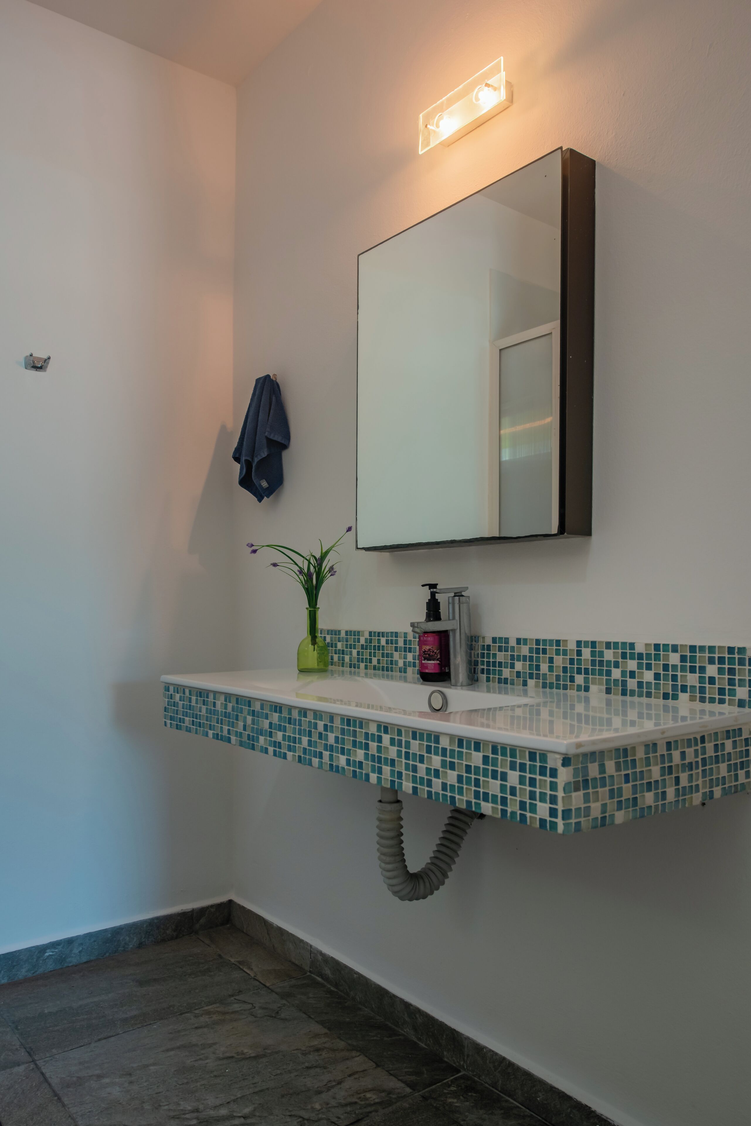 A bathroom with a tiled sink, a mirror, a towel hanging on the wall, and a plant on the sink.