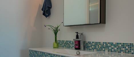 A bathroom with a tiled sink, a mirror, a towel hanging on the wall, and a plant on the sink.