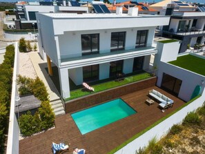 Una casa moderna a due piani con piscina, area salotto esterna e pannelli solari.