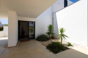 Ein modernes Äußeres mit Beton-Terrasse, Glastür und kleinem Garten mit Pflanzen.
