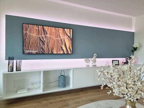 Ein modernes Wohnzimmer mit einem flachbildfernseher, der an einer grauen Wand angebracht ist, einer weißen Unterhaltungseinheit darunter und einem Holzboden.