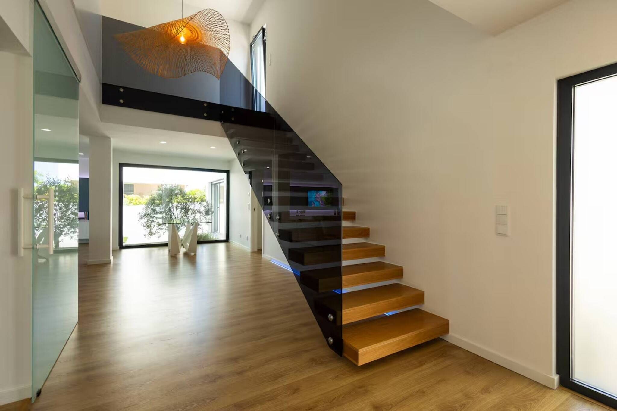 Ein modernes Interieur mit einer Holztreppe, Glastrennwand und einer Pendelleuchte.