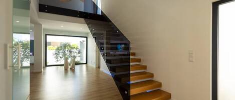 Um interior moderno com escada de madeira, guarda-corpo de vidro e luminária pendente.