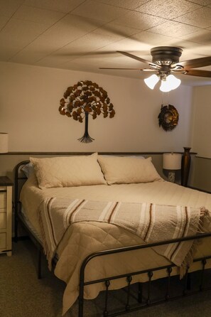 Ein Schlafzimmer mit einem Bett, einem Deckenventilator, einer Wanddekoration und einem Nachttisch.