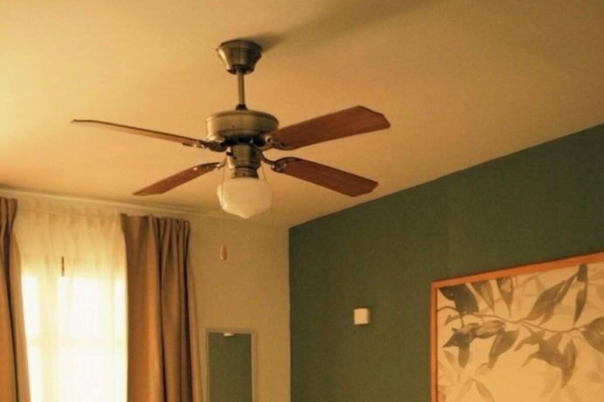 Habitación de hotel con cama, ventilador de techo, un cuadro en la pared y ventana con cortinas.