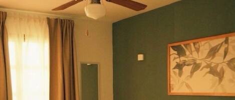 Habitación de hotel con cama, ventilador de techo, un cuadro en la pared y ventana con cortinas.