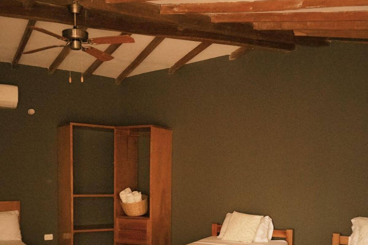 Una habitación con piso de madera, ventilador de techo y tres camas individuales.
