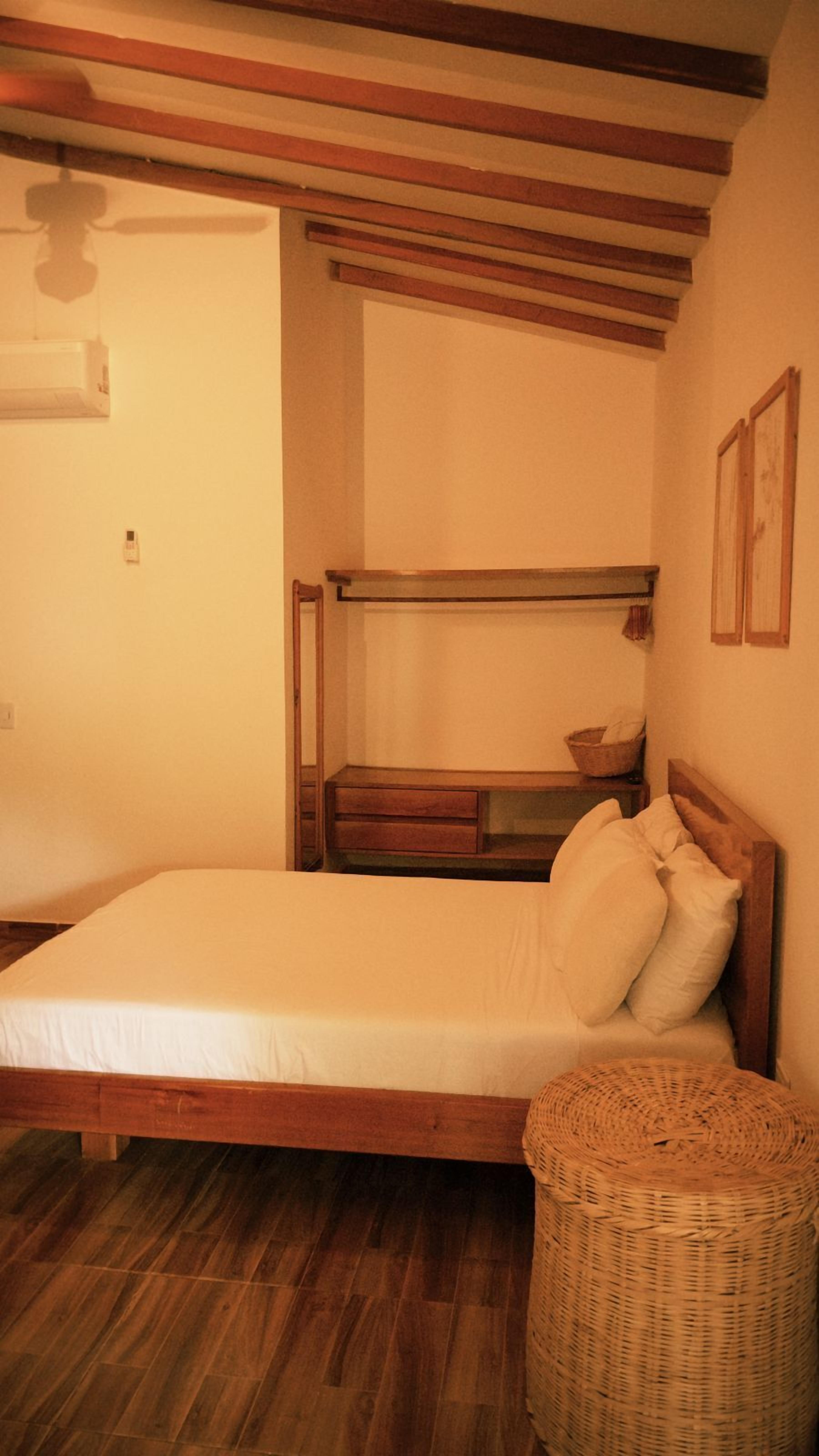 Una habitación con una cama nido de madera, una cama individual, una mesita de noche pequeña de madera, una cesta de mimbre y un aire acondicionado instalado en la pared.