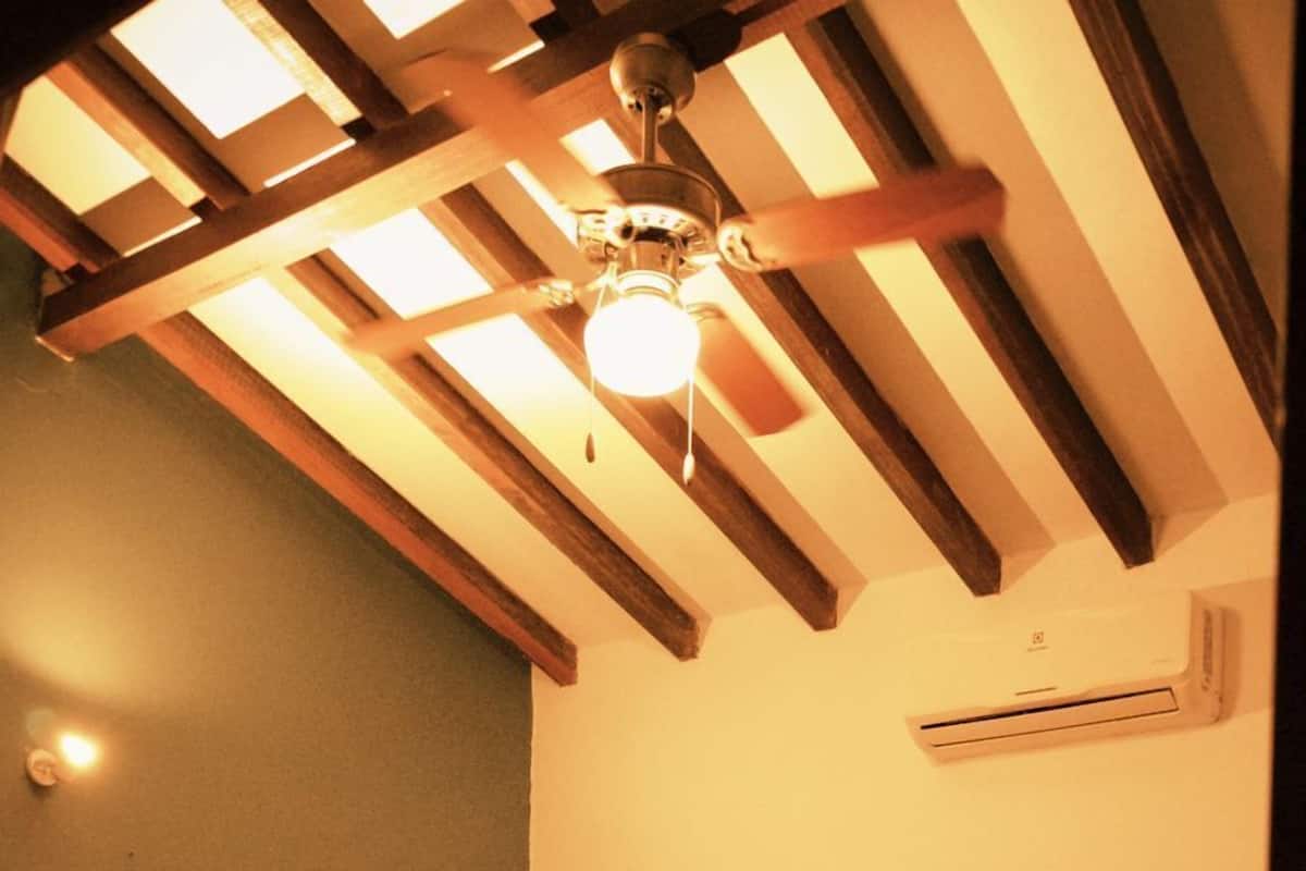 Una habitación pequeña con cama individual, techo inclinado, ventilador de techo y aire acondicionado.