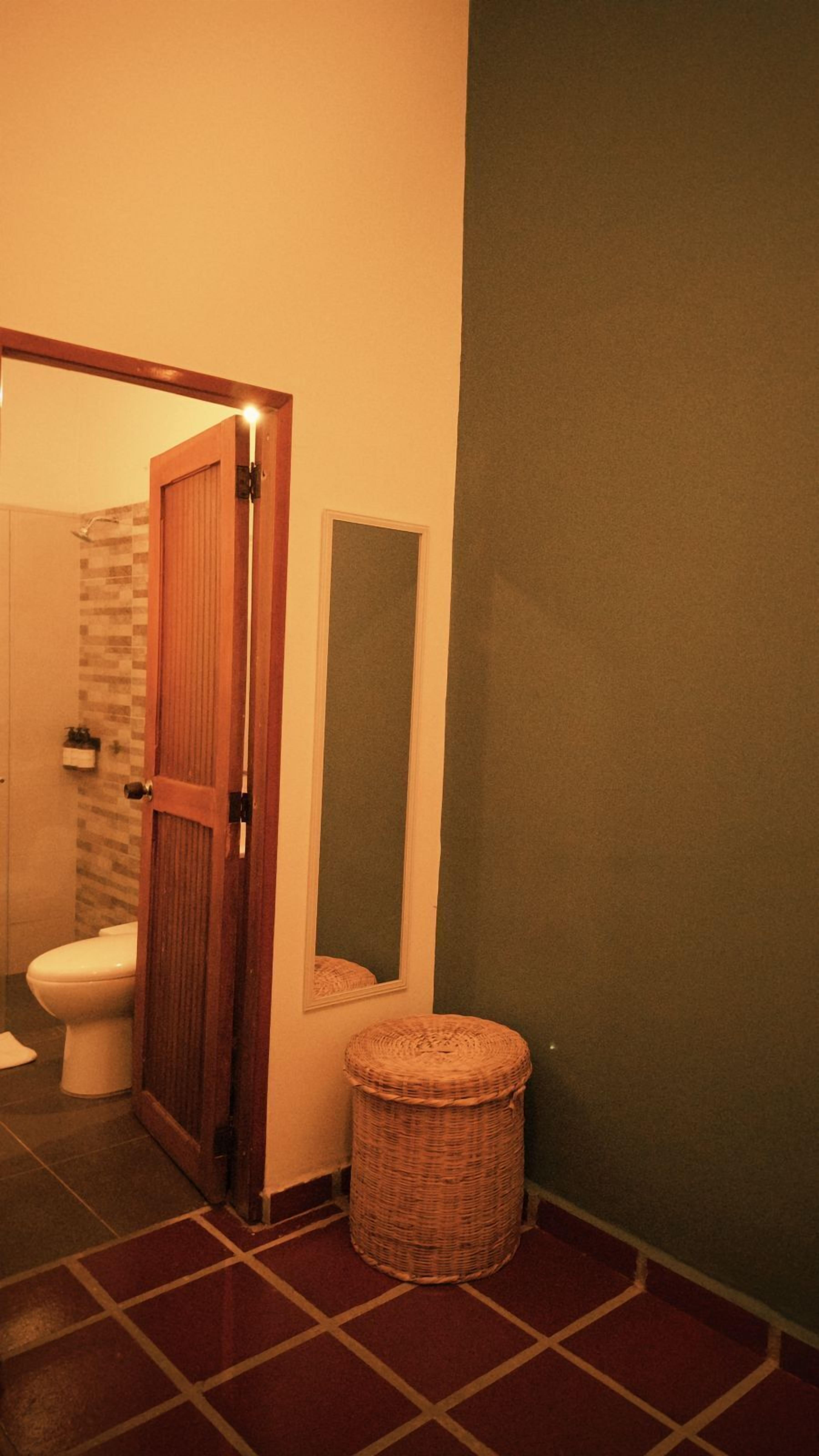 A bathroom with a toilet, a wicker waste basket, and a wooden door leading to a shower area.