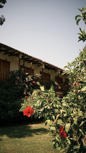 A building with a tiled roof, a covered porch, and a garden with red flowers. - Hotel Jardin Boutique Rodadero (Santa Marta)