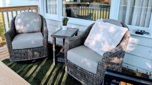 Eine überdachte Veranda mit Korbmöbeln, einem kleinen Tisch und Blick auf den Garten.