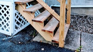 Eine Holztreppe führt zu einer Veranda mit weißer Geländer.