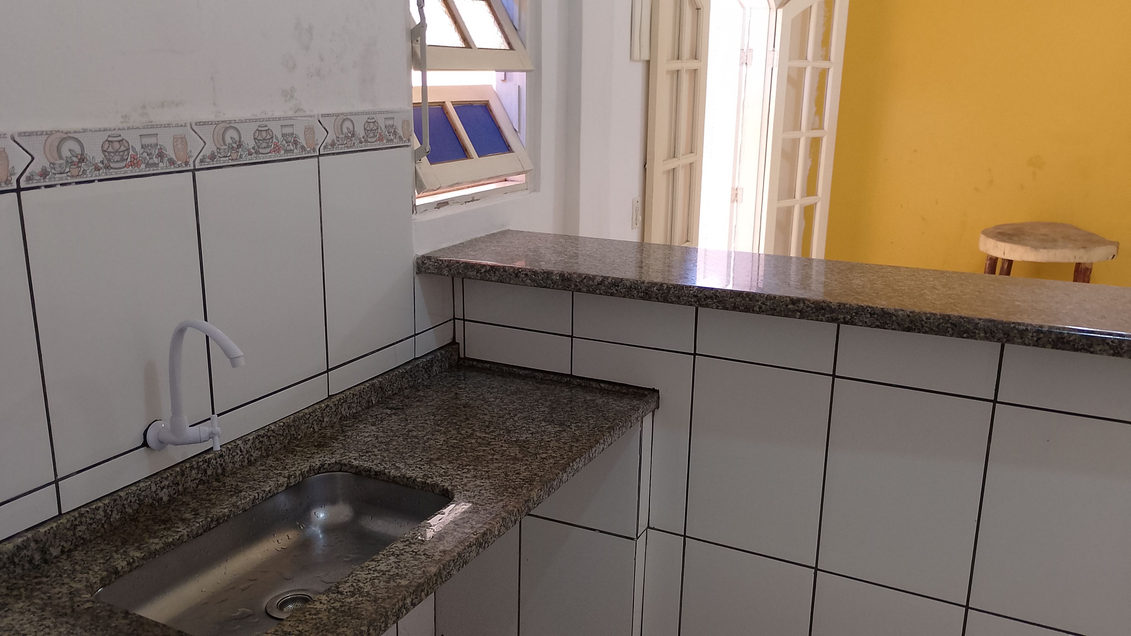 A kitchen with white tiles, a granite countertop, and a stainless steel sink.