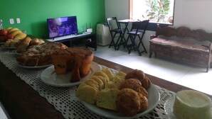 Ein Essbereich mit einem langen Tisch, gedeckt mit verschiedenen Backwaren, einem Fernseher und einem Fenster mit Gartenblick.