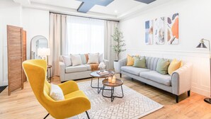 Uma sala de estar moderna com sofá, poltronas, mesa de centro e uma janela grande com cortinas.