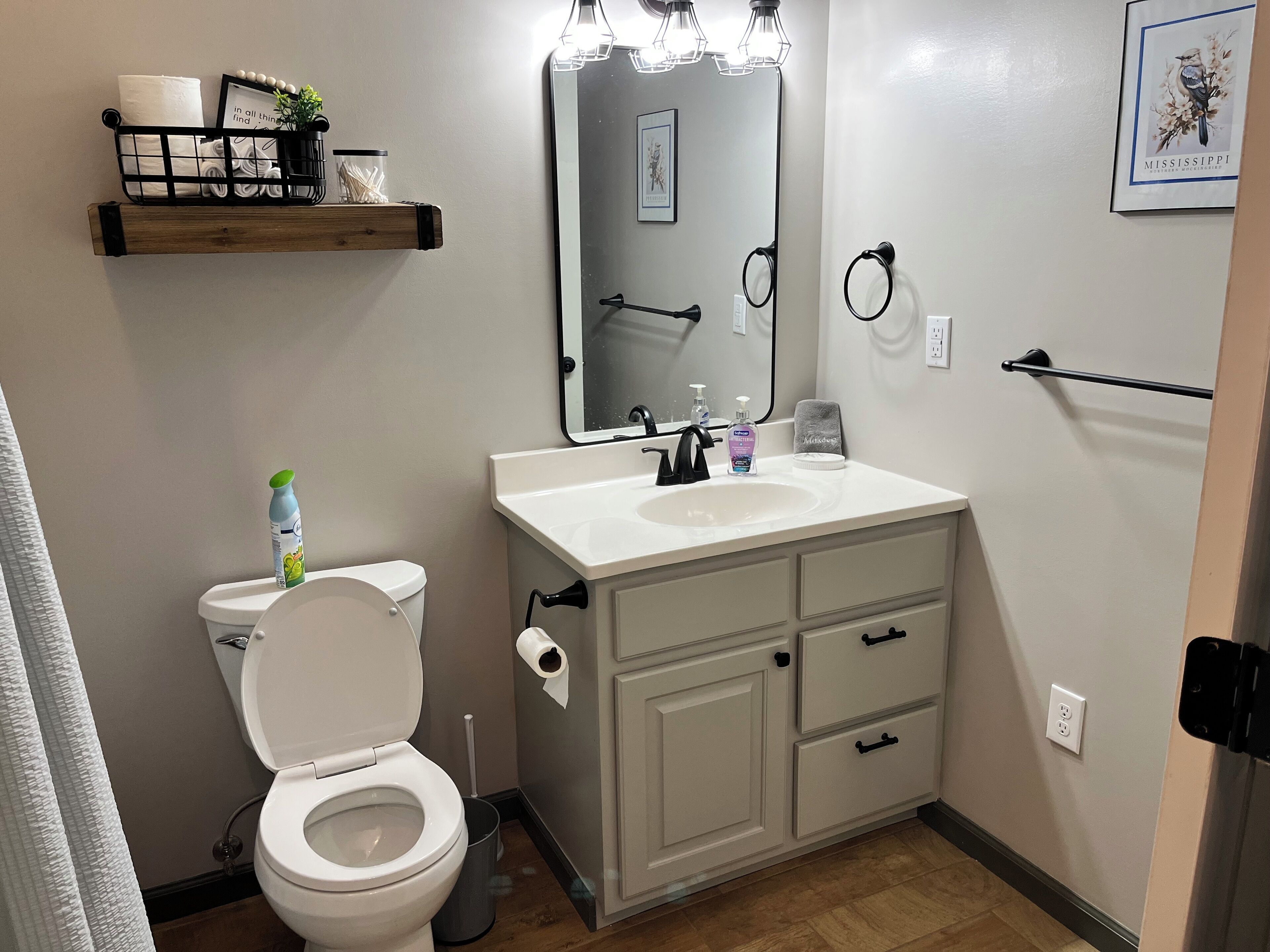 A bathroom with a toilet, sink, vanity, and a mirror with lights.
