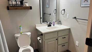 A bathroom with a toilet, sink, vanity, and a mirror with lights.