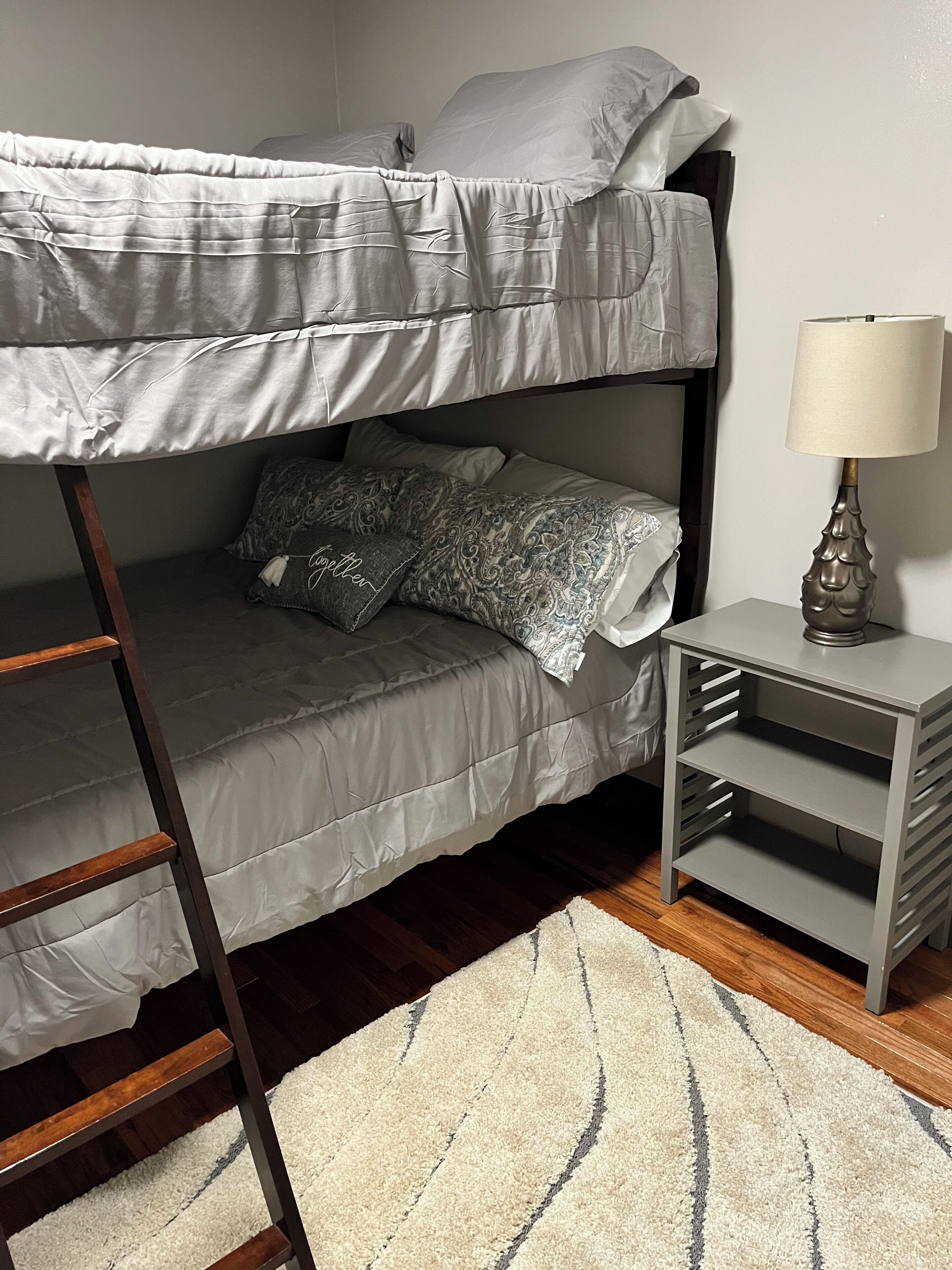 A bunk bed with a ladder, a bedside table with a lamp, and a patterned rug.
