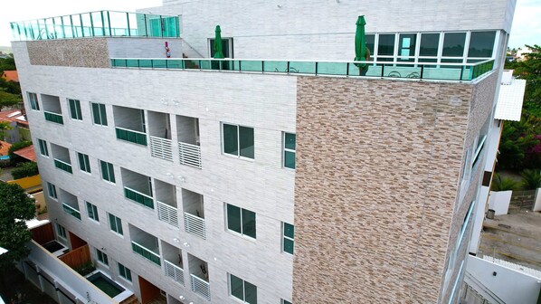 Un immeuble à plusieurs étages dont la façade est un mélange de briques et de verre, doté de balcons et d’une terrasse sur le toit.