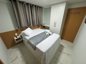 A hotel room with a bed, a bedside table, a wardrobe, and a door.