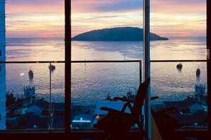 Vista desde una habitación de hotel en un rascacielos, con una masa de agua y una isla a lo lejos, mostrando una silla y una mesa en primer plano.