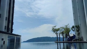 A modern building with a glass facade overlooking a calm body of water and distant hills. - Seaview Bliss Studio By Tropical Elegance (Kota Kinabalu)