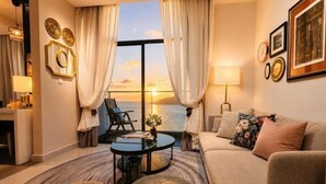 A living room with a sofa, a coffee table, a chair, and a view of the sunset through large windows. - Seaview Bliss Studio By Tropical Elegance (Kota Kinabalu)