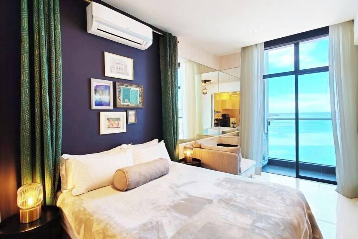 Een hotelkamer met een bed, een bureau, een stoel, een groot raam en uitzicht op zee.