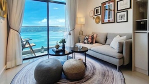 A modern living room with a large window, a sofa, a coffee table, and decorative items. - Seaview Bliss Studio By Tropical Elegance (Kota Kinabalu)