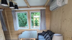 A cozy room with a wooden ceiling, a dining table with chairs, a sofa, and a lamp. There are windows with curtains and a view of greenery outside. - Chalet "pied aigu" At the foot of the Vercors, mountains and hiking. Pets allowed  (Rovon)