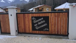 A wooden gate with a sign that reads "Bienvenue aux chalets Rovonnais" in front of a building with a white roof, surrounded by mountains. - Chalet "pied aigu" At the foot of the Vercors, mountains and hiking. Pets allowed  (Rovon)