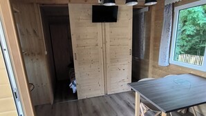 A wooden interior with a table and chairs, a TV mounted on a wooden door, and a window with a view of trees. - Chalet "pied aigu" At the foot of the Vercors, mountains and hiking. Pets allowed  (Rovon)