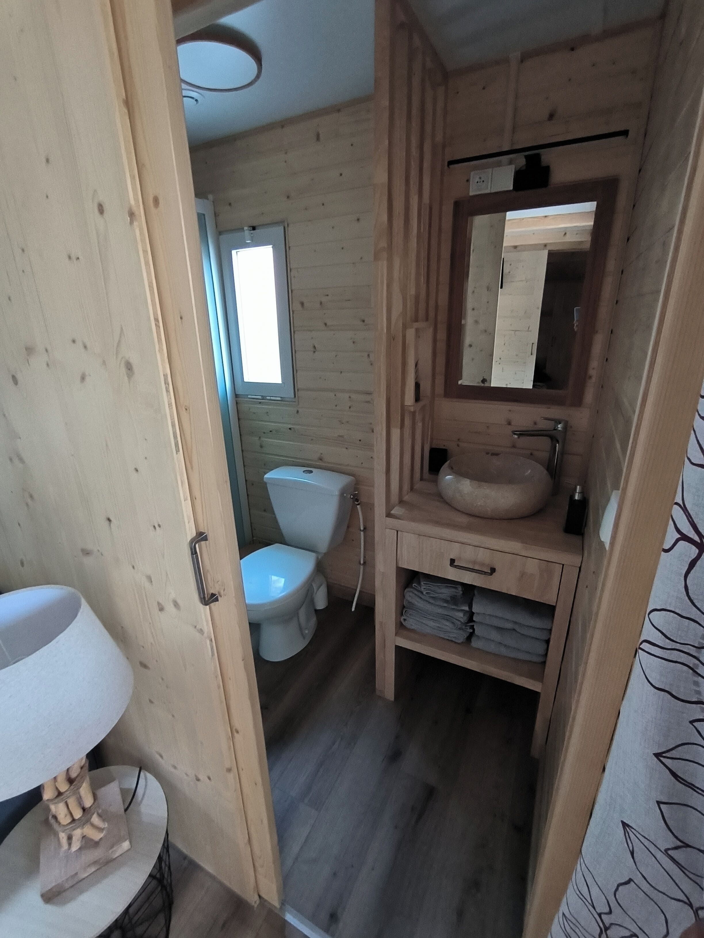 Et badeværelse i en træhytte med toilet, vask og spejl.