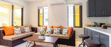 A modern living room with a sofa set, a coffee table, and a kitchen area with bar stools.
