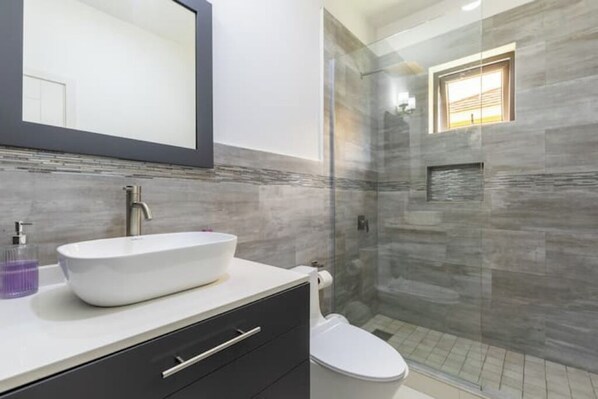 A modern bathroom with a large mirror, a white sink, and a glass-enclosed shower.