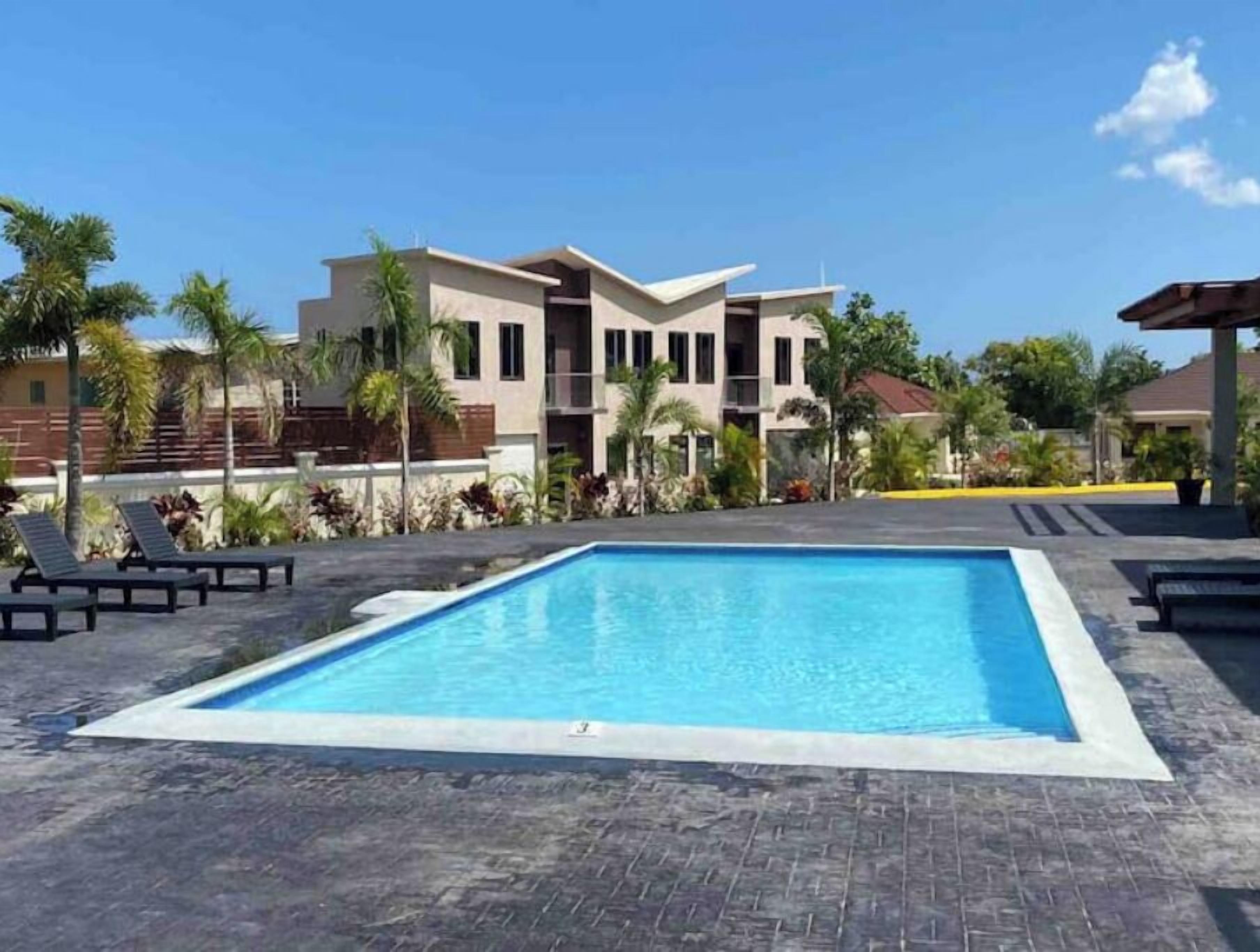 A swimming pool with lounge chairs, surrounded by palm trees and a modern building in the background.
