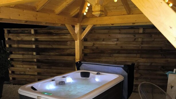 A hot tub in an outdoor wooden cabin with a tiled floor and two wicker chairs.