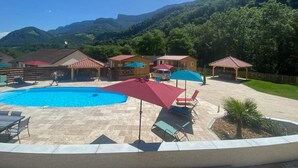 A pool area with lounge chairs and umbrellas, surrounded by buildings and a mountainous backdrop.