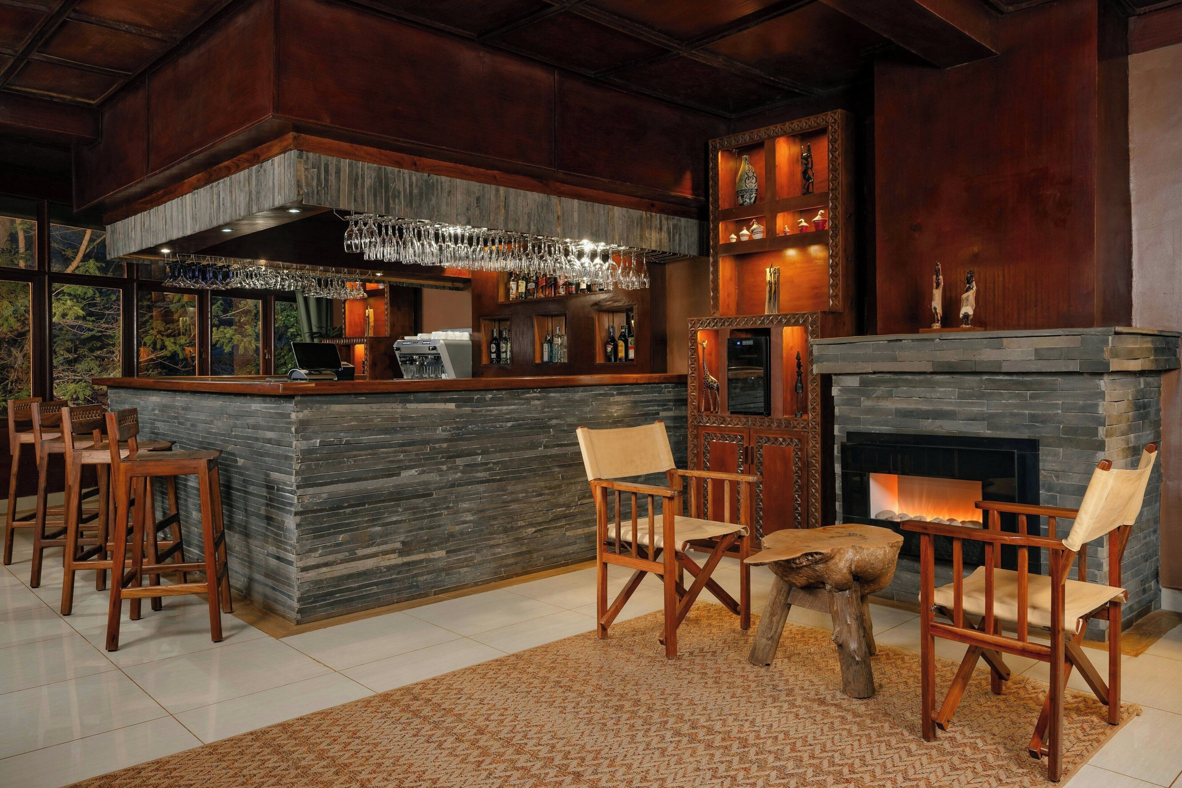 A bar area with a stone counter, wooden chairs, a fireplace, and a view of the outdoors.