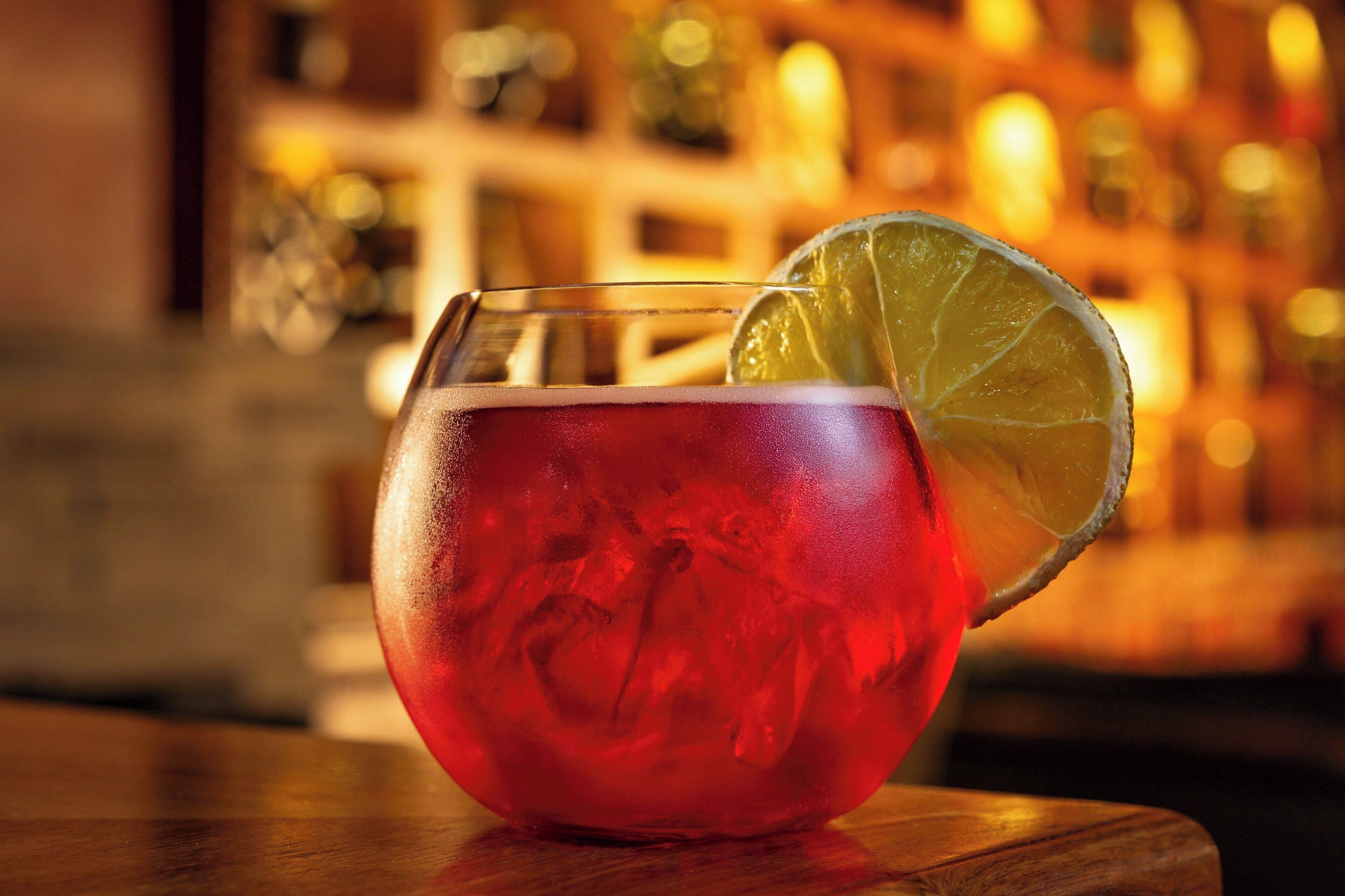 A glass of red beverage with a lime slice on a wooden surface.