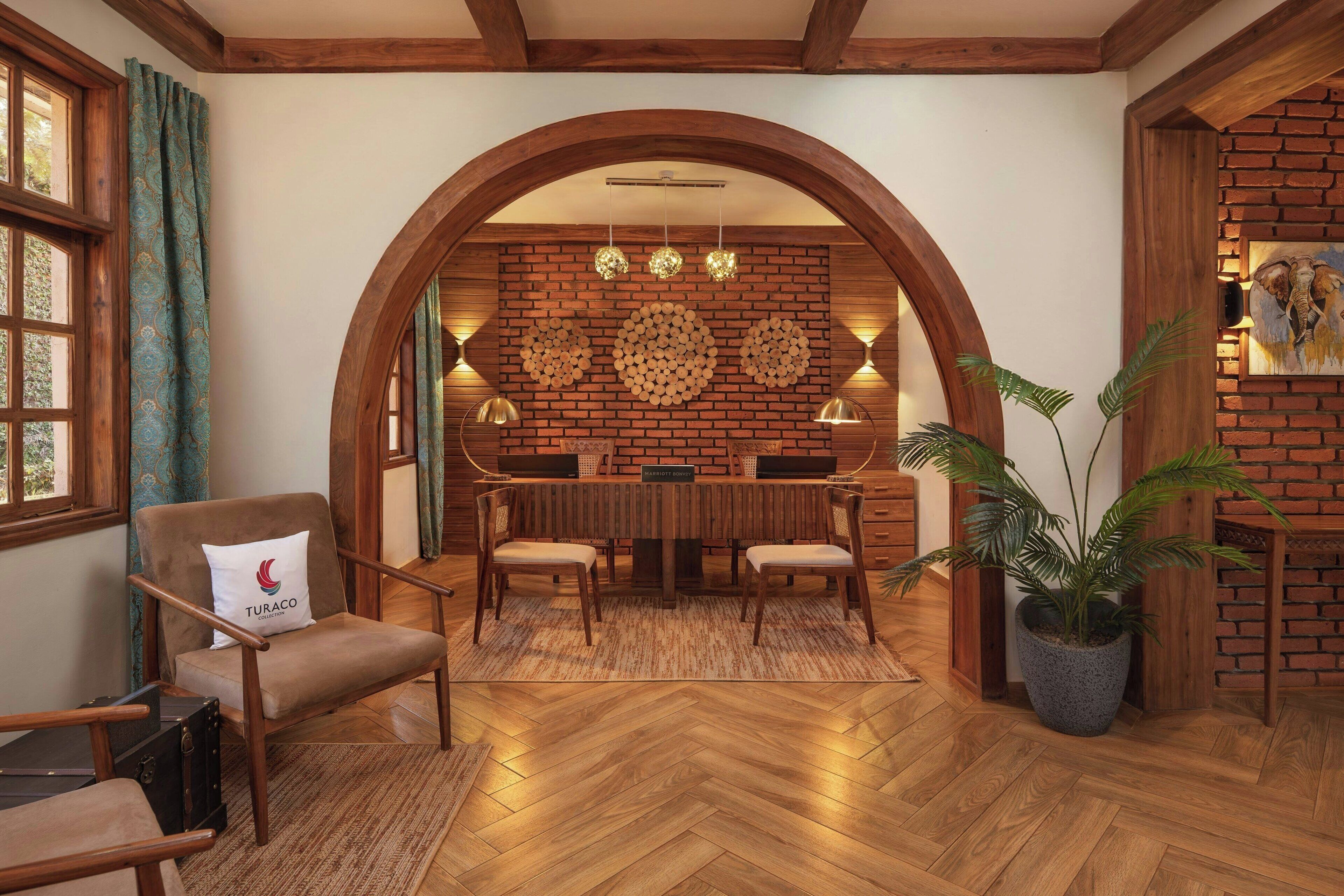 A cozy room with a wooden floor, a dining table with chairs, a sofa with a pillow, a potted plant, and a brick wall with a wooden archway.