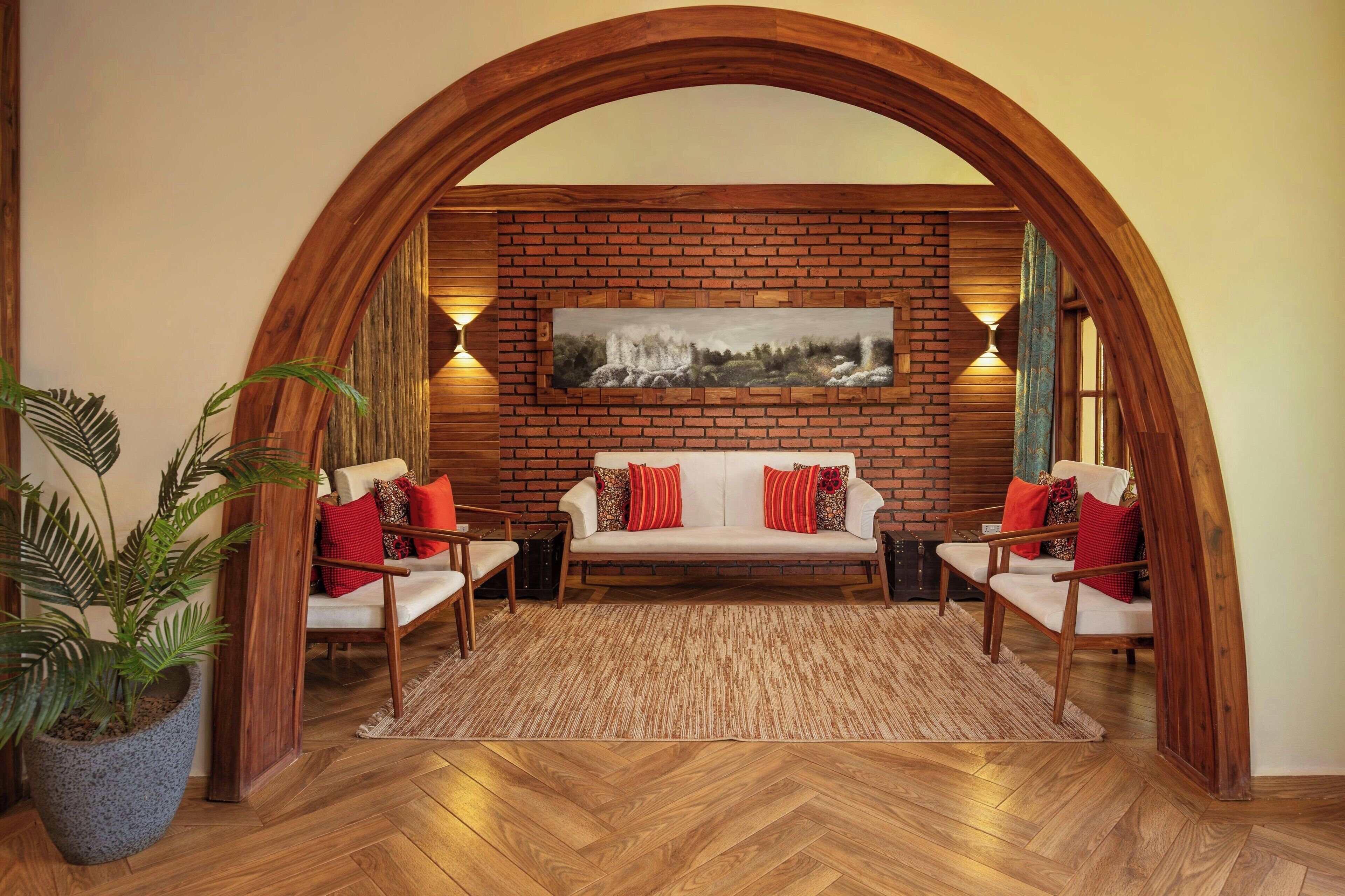 Una habitación acogedora con pared de ladrillo, un sofá blanco, dos sillones, un cuadro grande y un arco de madera.