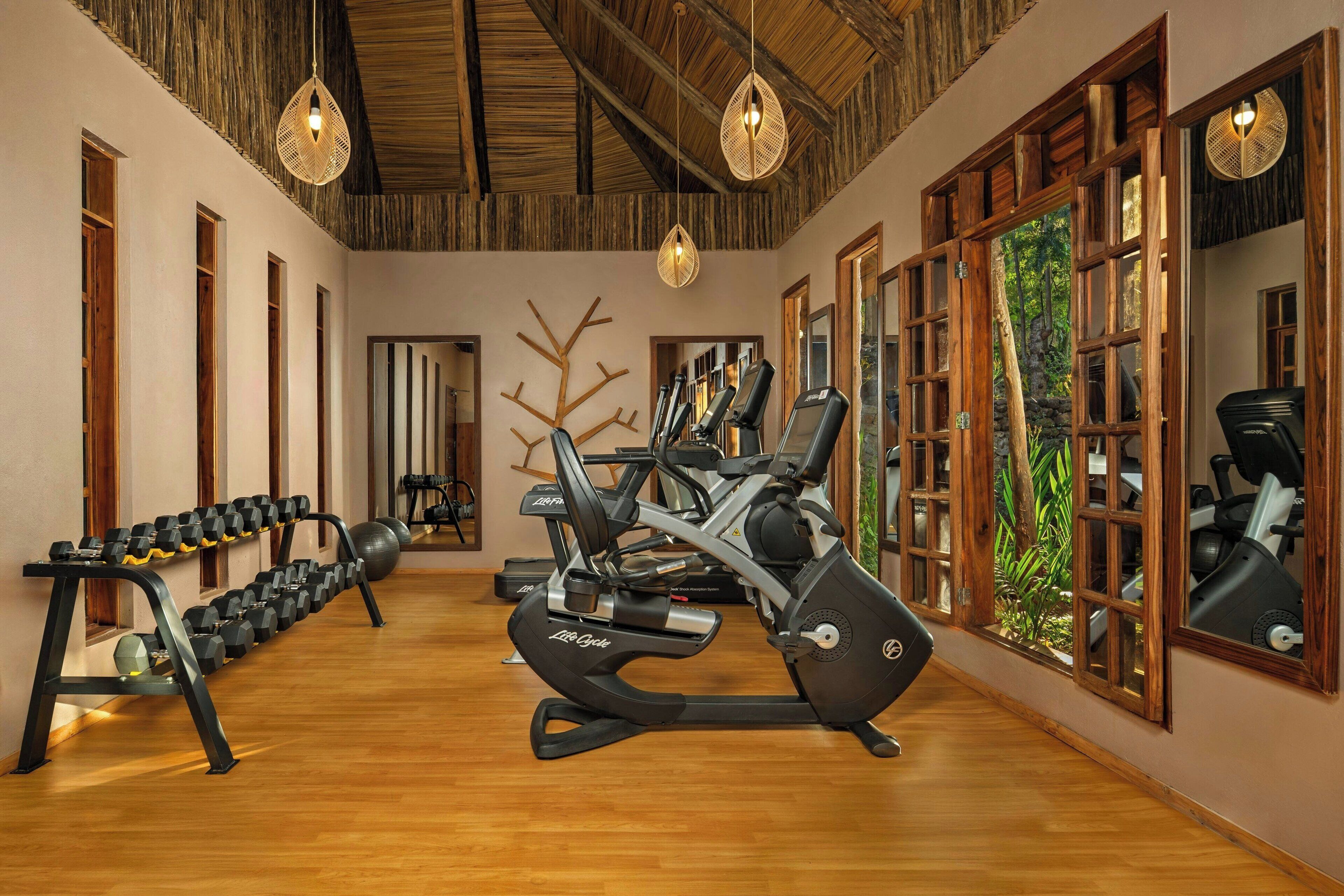 A gym with exercise equipment, wooden flooring, and large windows.