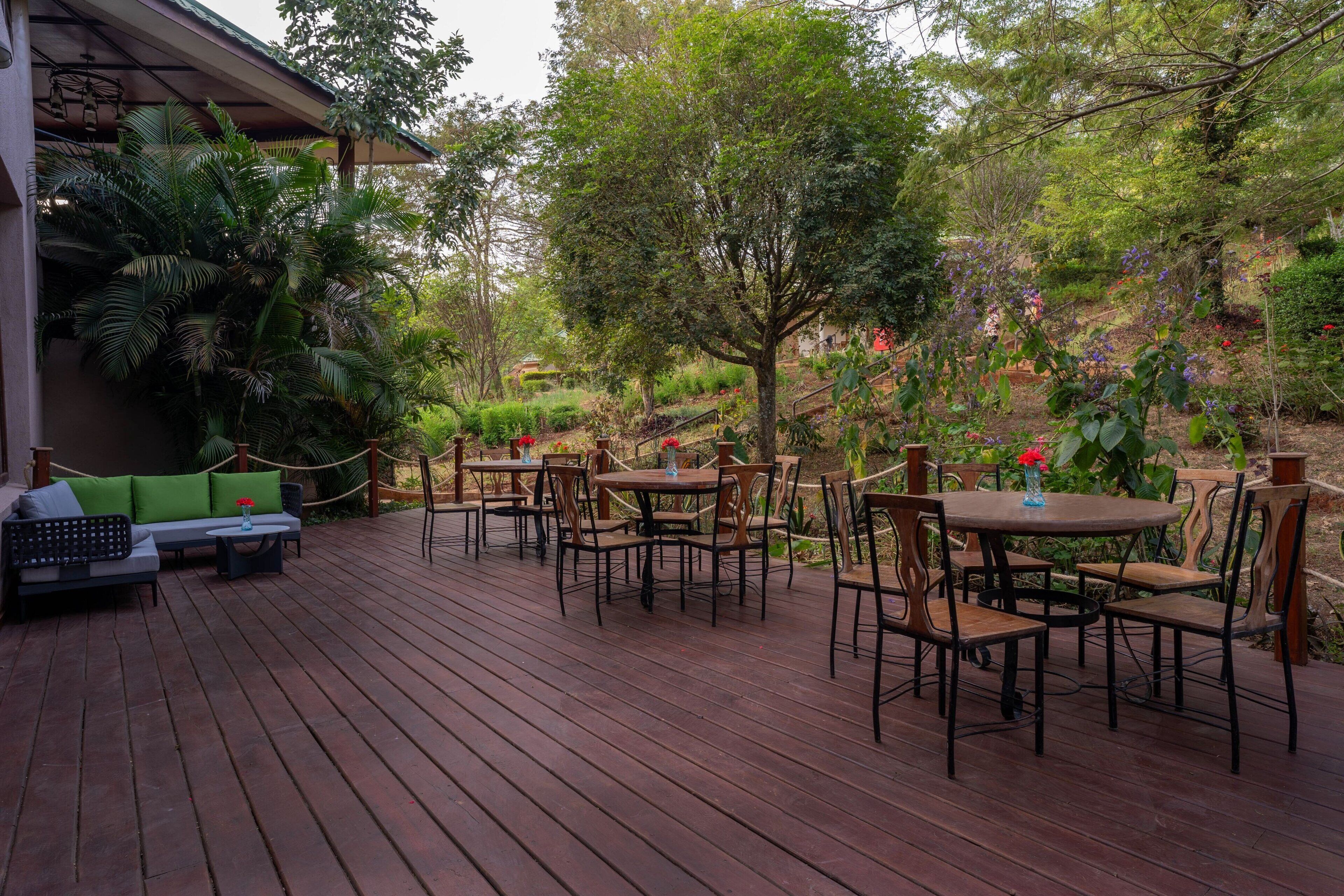 Una terraza de madera con mobiliario exterior y abundante vegetación.