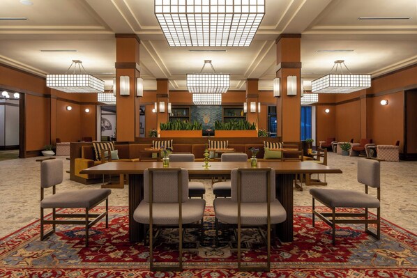 Un vestíbulo amplio con una mesa de comedor central rodeada de sillas, una alfombra estampada y lámparas modernas.